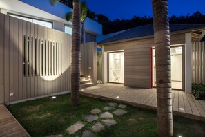 A modern house with a wooden deck, a grassy area with stepping stones, and a well-lit interior. - Villa Angelique  | Ocean View - Located in  Wonderful Saint Jean with Private Pool (Saint Barthélemy)