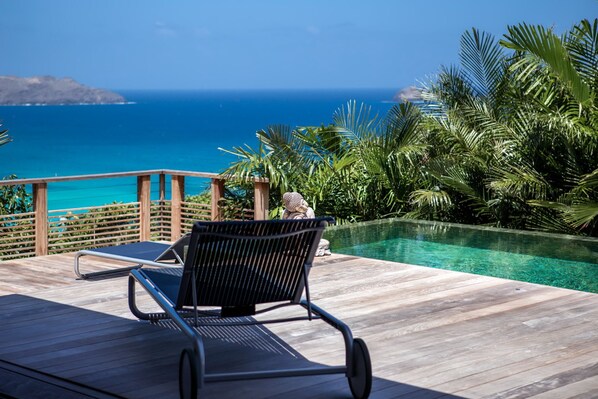 A wooden deck with a lounge chair, a pool, and a view of the ocean. - Villa Angelique  | Ocean View - Located in  Wonderful Saint Jean with Private Pool (Saint Barthélemy)