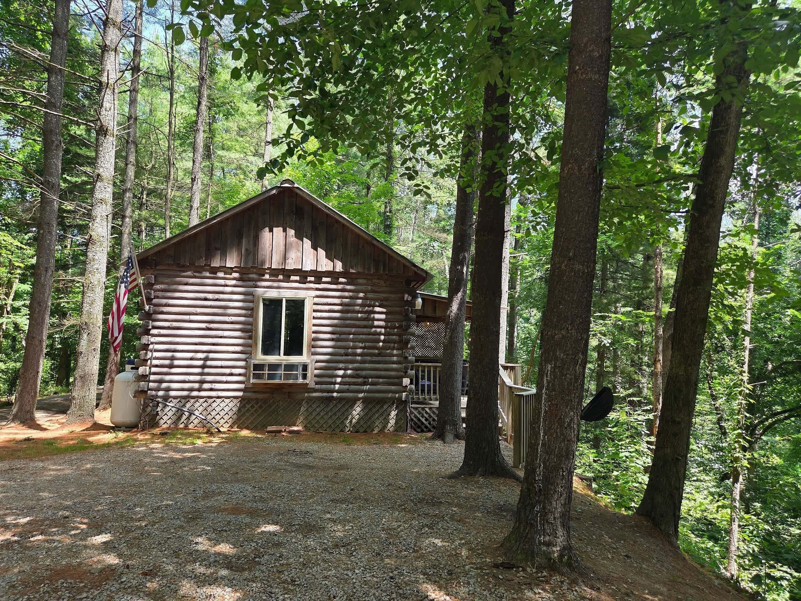 A rustic log cabin with a window and a door, surrounded by trees.