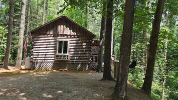 A rustic log cabin with a window and a door, surrounded by trees.