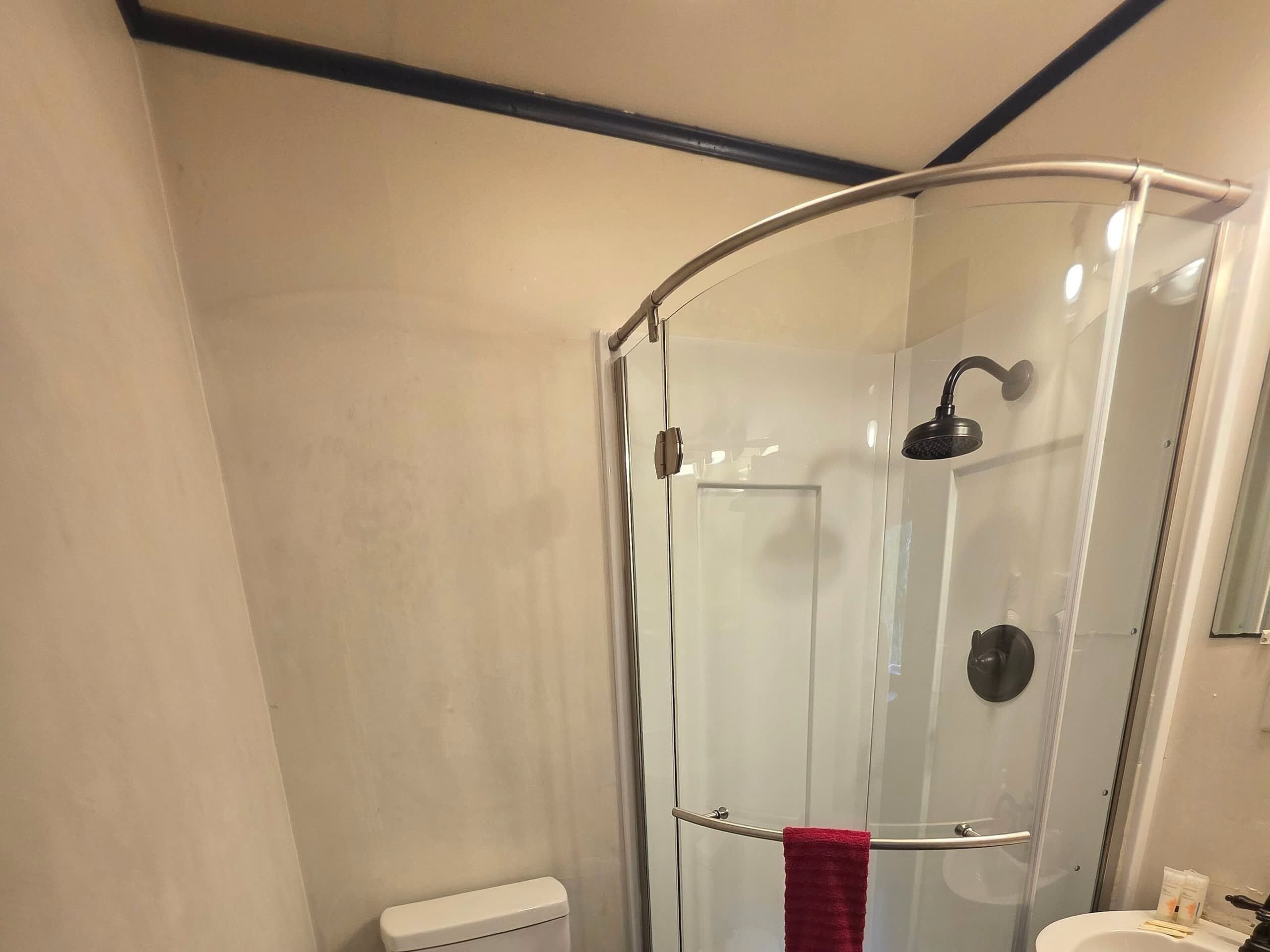 Um chuveiro com paredes de vidro e porta curva, um vaso sanitário branco e uma pia com uma toalha vermelha pendurada na porta.