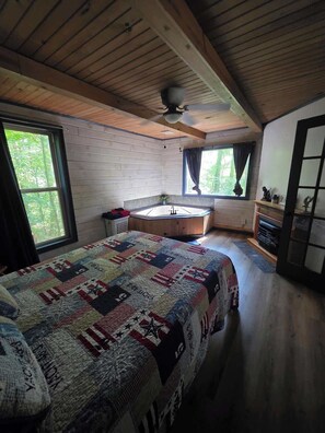 Ein Interieur einer Hütte mit Bett, Fenster, Deckenventilator und kleinem Badezimmer.