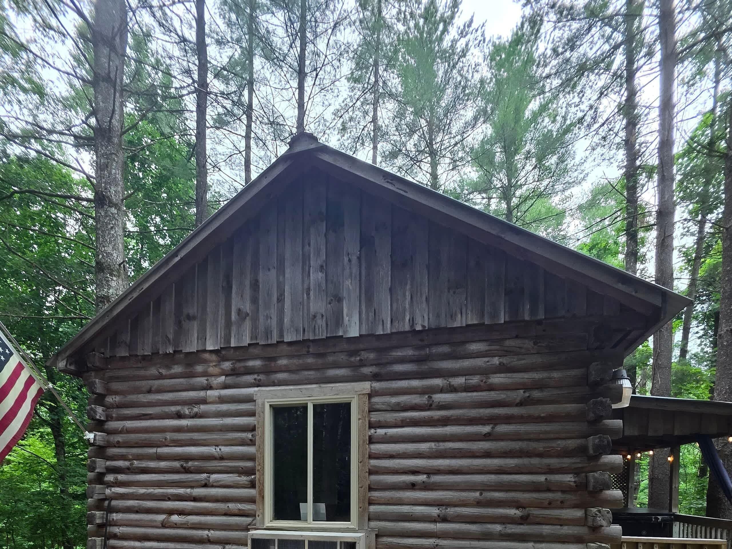 A log cabin with a pitched roof, a window, and an American flag.