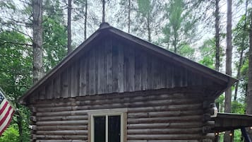 A log cabin with a pitched roof, a window, and an American flag.