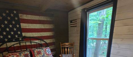 Un dormitorio con una cama, una silla, un ventanal y una pared con una bandera.