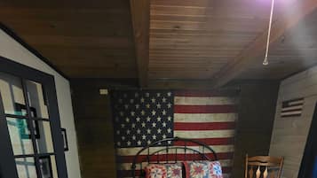 Et soveværelse med en seng, trælofter, en væg med et amerikansk flag og en stol med pude formet som en cykel.