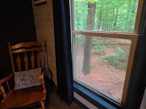 Une chaise en bois avec un coussin à rayures et une fenêtre donnant sur une forêt.
