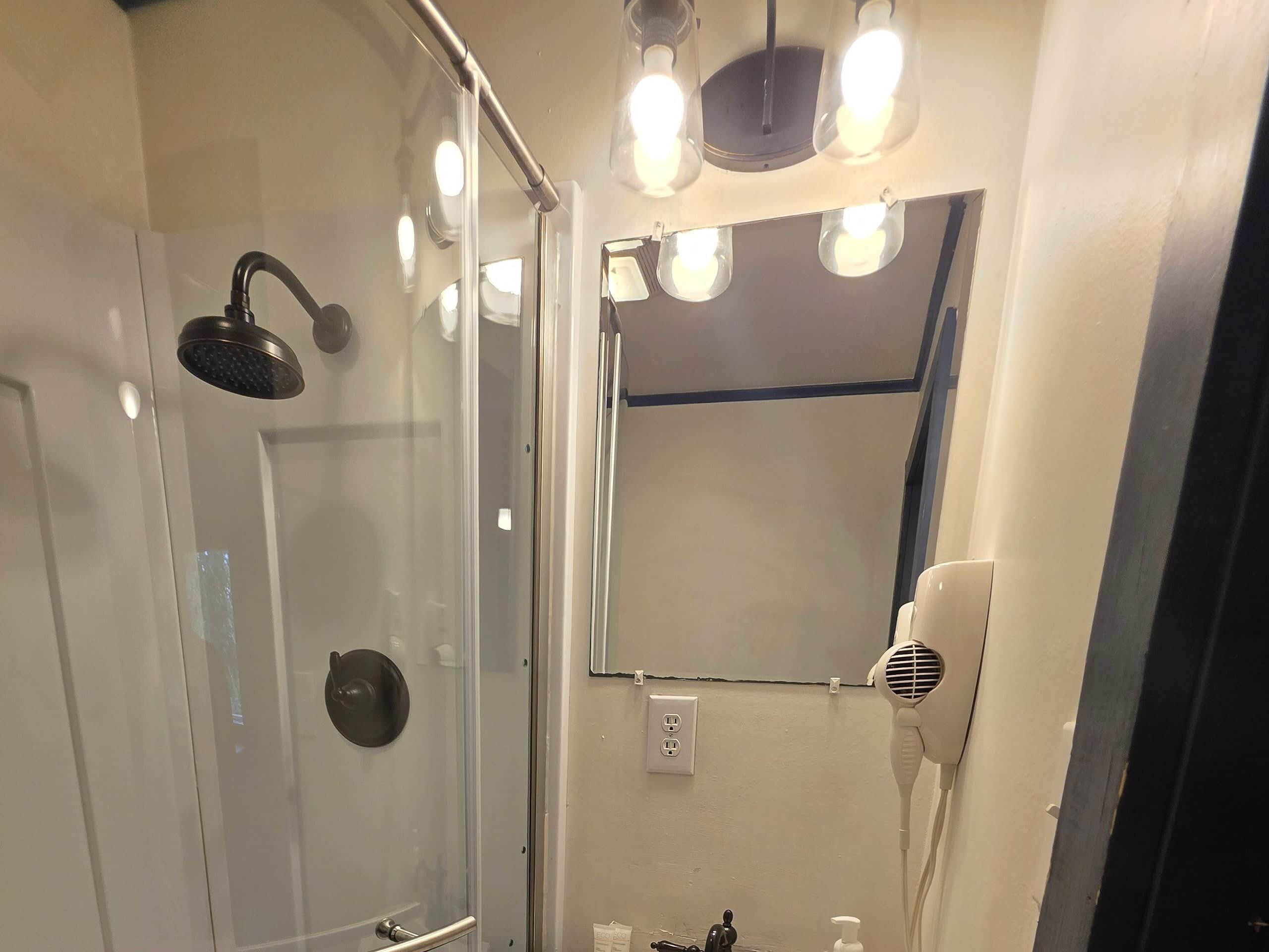 Een badkamer met een douchecabine van glas, een haardroger en een spiegel.