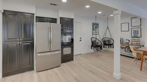 Uma cozinha moderna com eletrodomésticos de aço inoxidável, armários escuros e uma área de refeições com mesa e cadeiras.