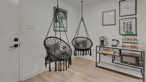 Quarto moderno com porta branca, duas cadeiras penduradas, máquina de café, micro-ondas e uma estante com livros e uma caixa rotulada 'STASH'.