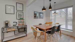 Uma área de refeições com mesa de madeira, cadeiras pretas e bege, luminárias pendentes e quadros nas paredes.