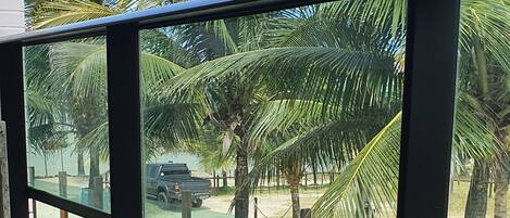 A balcony with a glass table and wicker furniture, overlooking a palm tree-lined area with a parked vehicle.