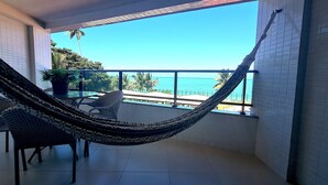 Un balcón con una hamaca, sillas y vista al océano.