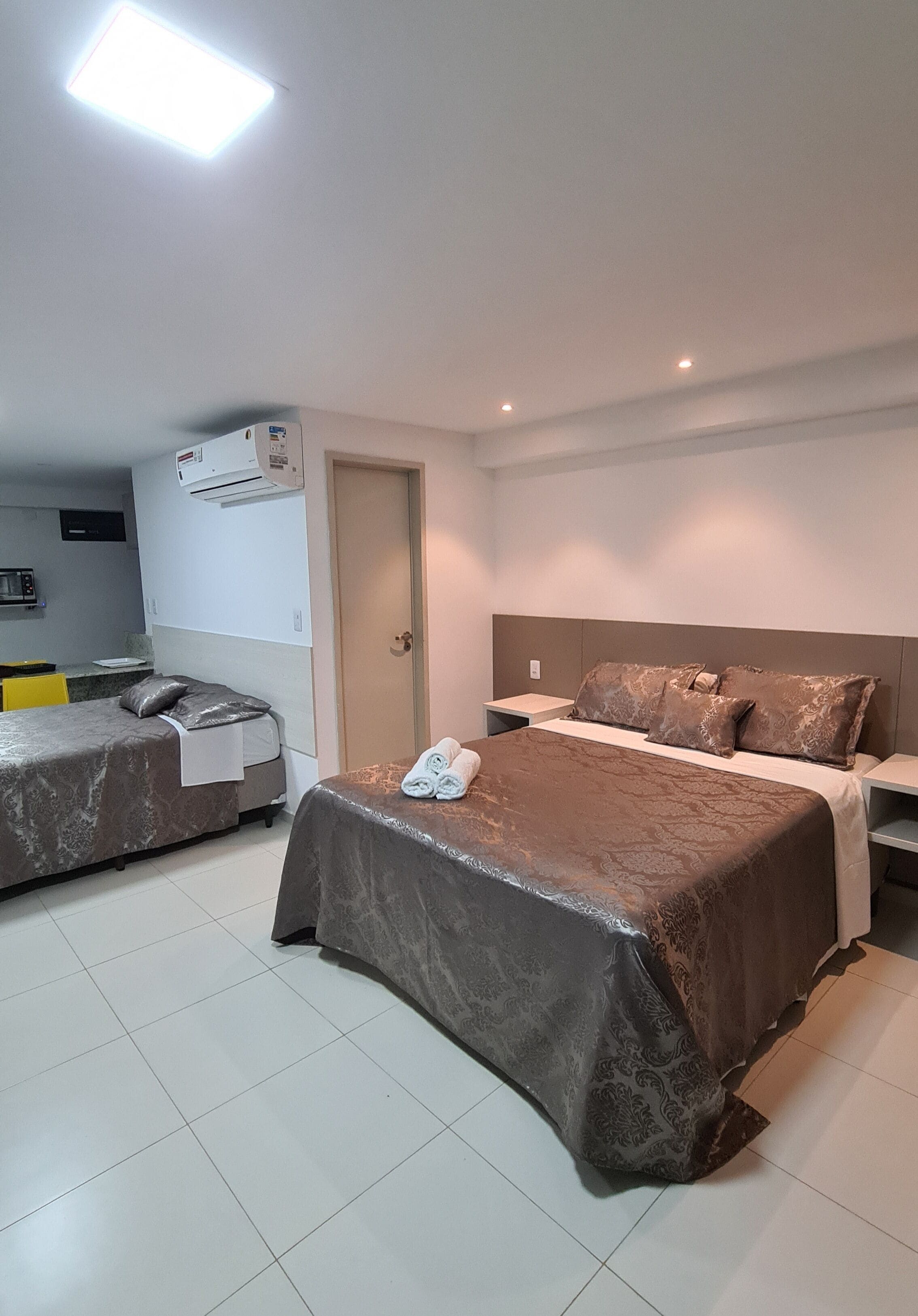 A hotel room with two beds, a kitchenette, and a door.