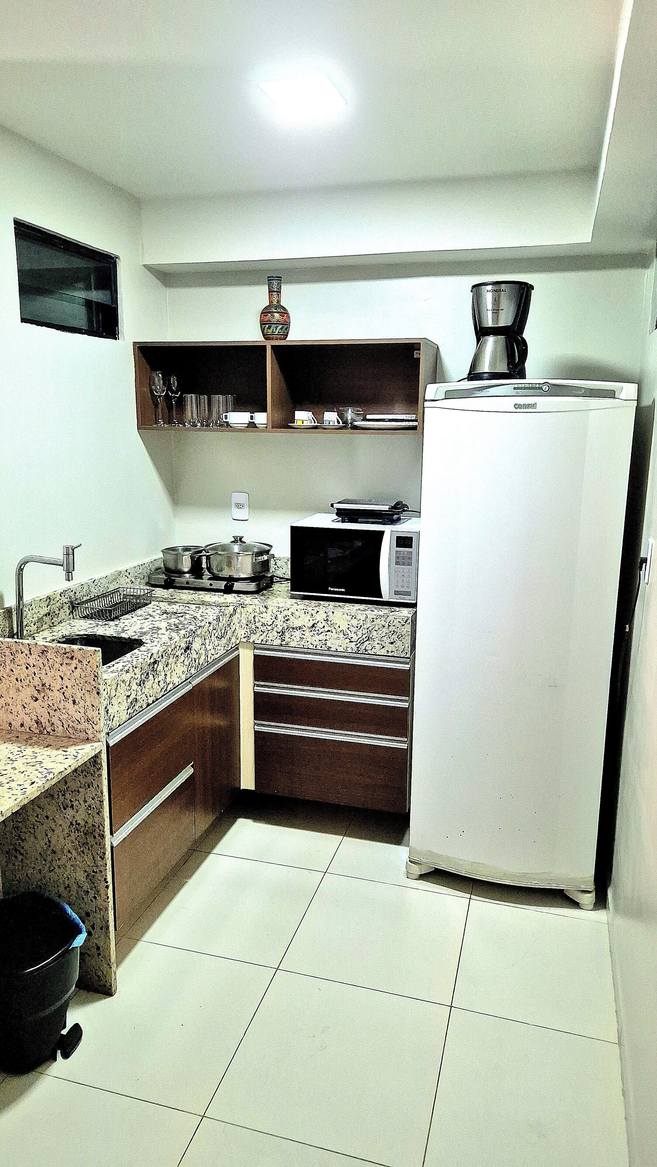 A compact kitchen with a refrigerator, microwave, sink, and a small shelf with a coffee maker.