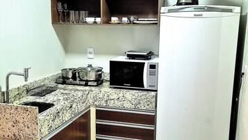 A compact kitchen with a refrigerator, microwave, sink, and a small shelf with a coffee maker.