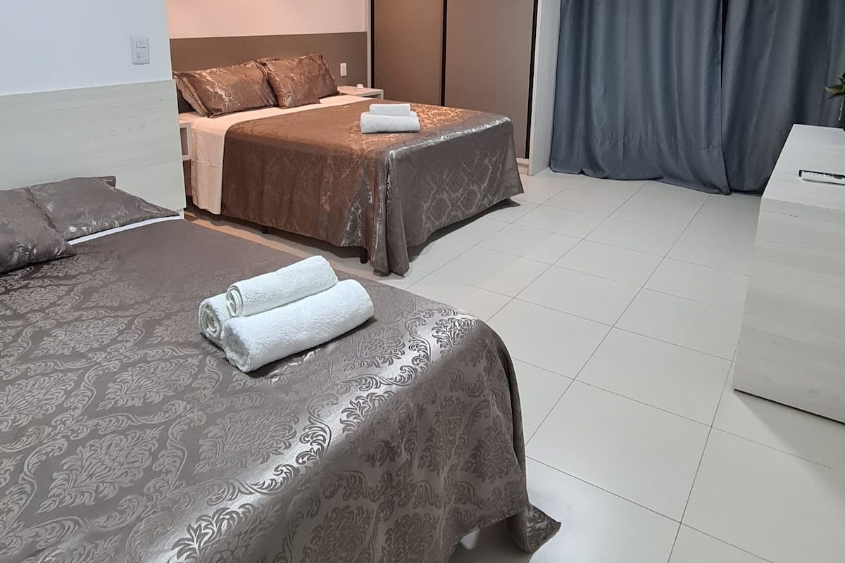 A hotel room with two beds, a desk, and a large window with curtains.