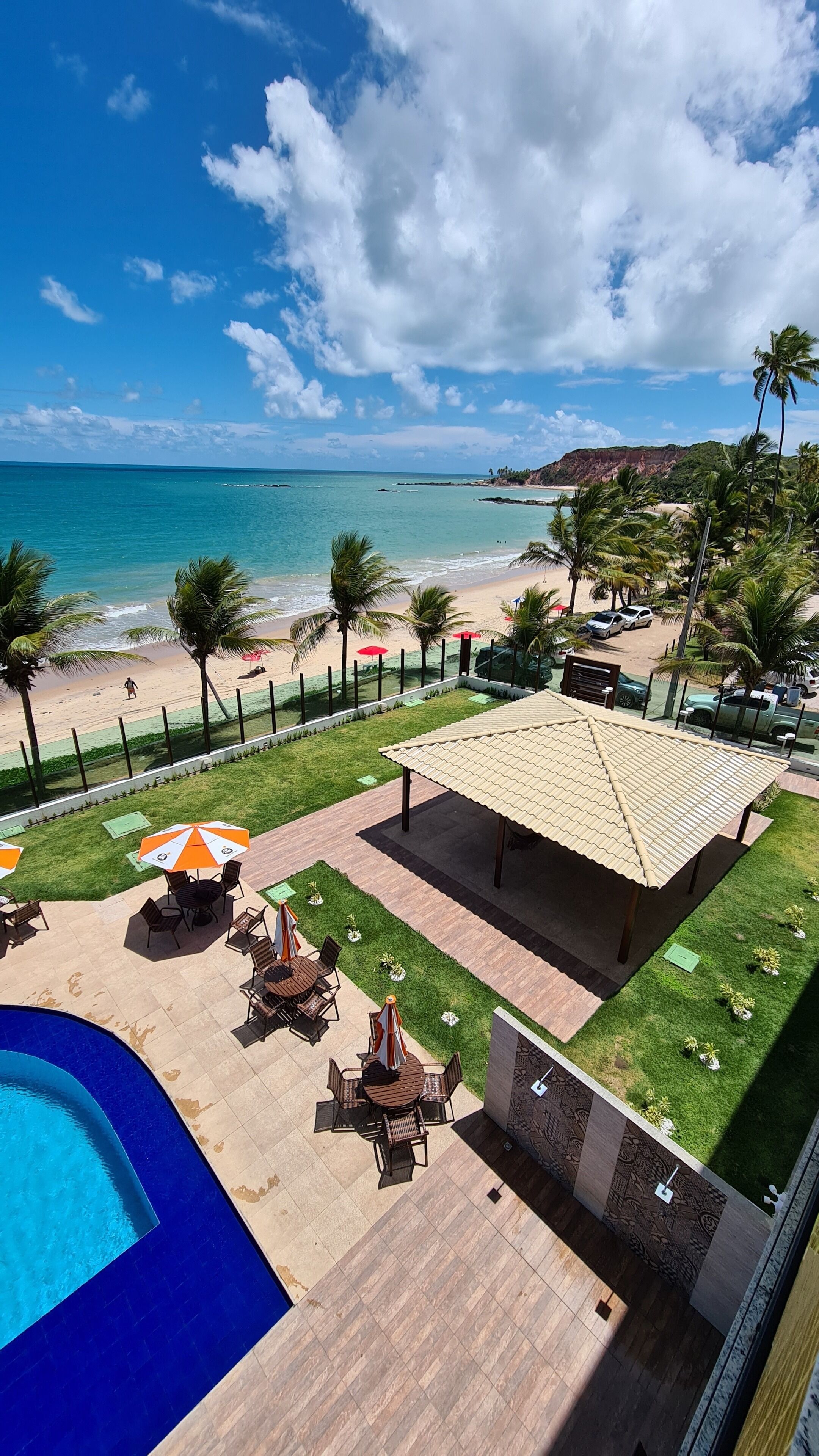 A pool area with a covered seating area, a beach view, and a fenced section with palm trees.