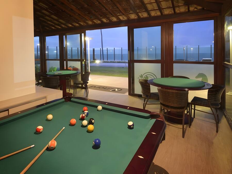 A pool table with balls, a green pool table, and a view of the ocean through large windows.
