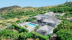 A large house with a swimming pool, surrounded by lush greenery and hills.