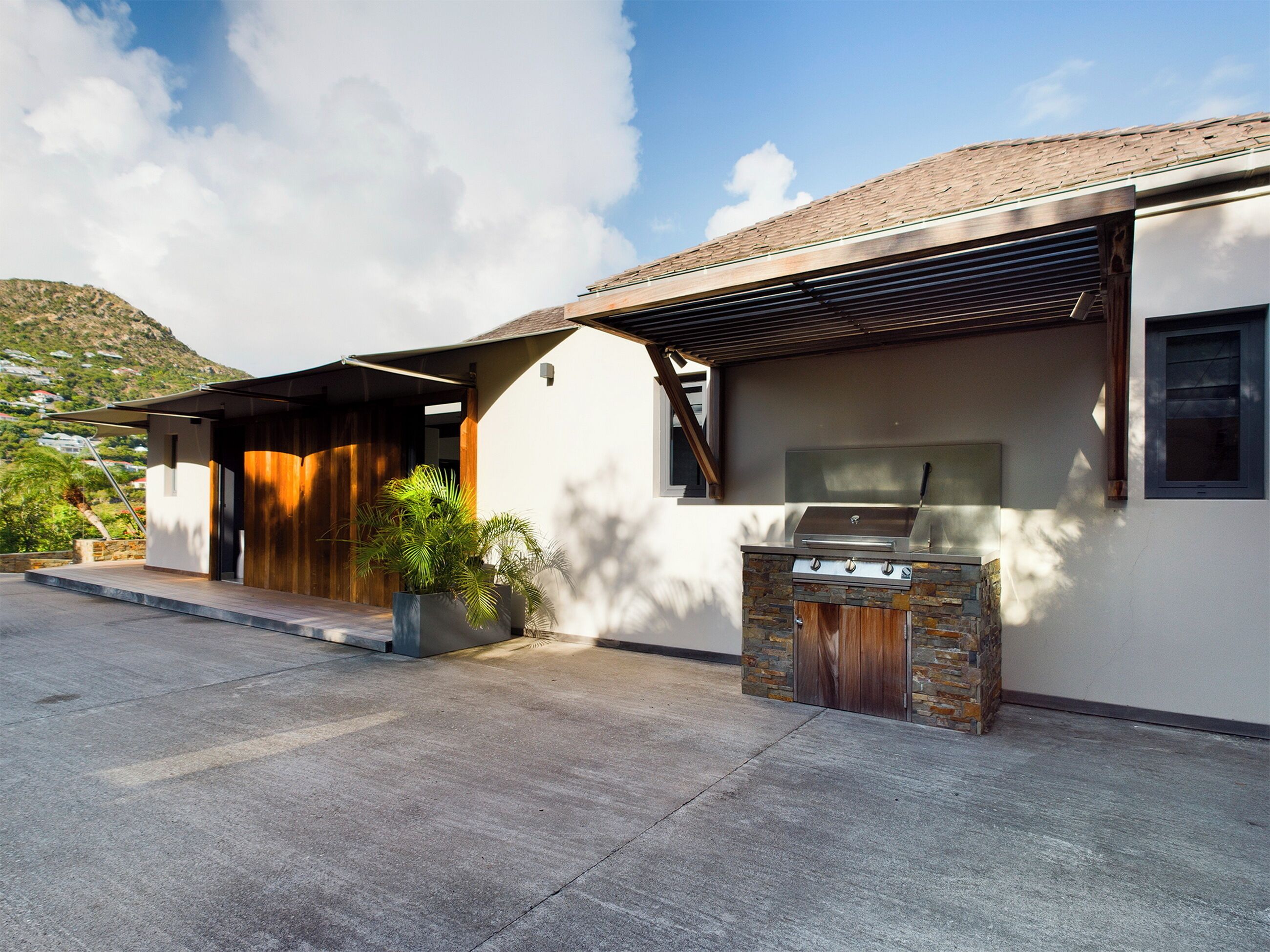 Une maison moderne dotée d’un patio, d’un barbecue et offrant une vue sur un paysage vallonné.