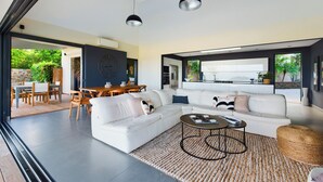 Een moderne woonkamer met een witte bank, een salontafel en een eethoek met een houten tafel en stoelen.