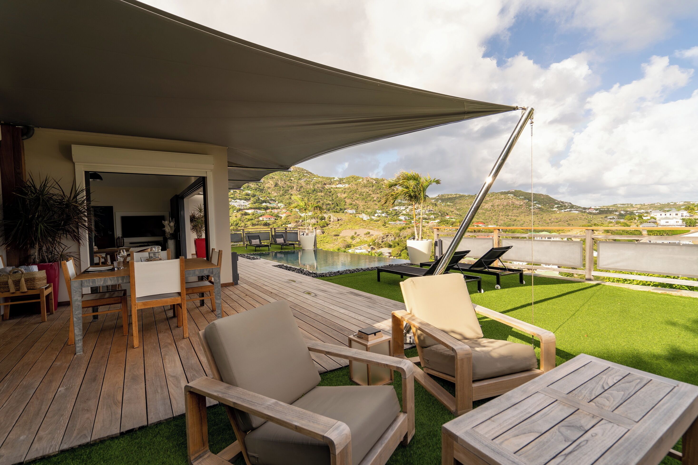 A wooden deck with outdoor furniture, a pool, and a view of a hillside.