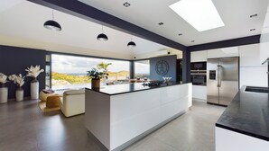 Een moderne keuken met een centraal eiland, een groot raam met uitzicht, hanglampen en inbouwapparatuur.