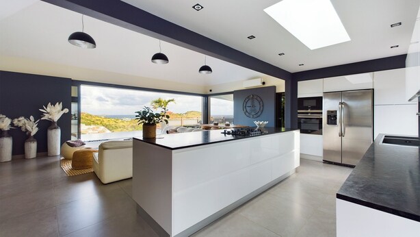 Une cuisine moderne dotée d’un îlot central, d’une grande fenêtre offrant une vue dégagée, de luminaires suspendus et d’appareils électroménagers intégrés.