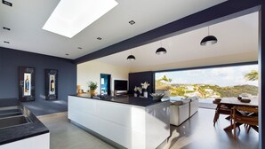 Een moderne keuken met een centraal eiland, een eethoek met uitzicht en een woonruimte met een groot raam dat uitkijkt op het landschap.