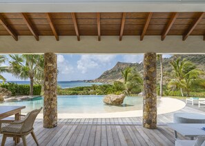 A wooden deck with a pool, stone pillars, and a view of the ocean and mountains. - Villa La Roche dans l’Eau | Ocean View - Located in  Exquisite Grand Fond with Private Pool (Grand Fond)