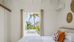 Un dormitorio con una cama, vista a palmeras y montañas, y un equipo de aire acondicionado.