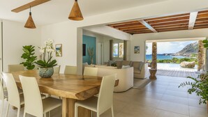 Un comedor moderno con una mesa y sillas de madera, un sofá y vistas al océano.