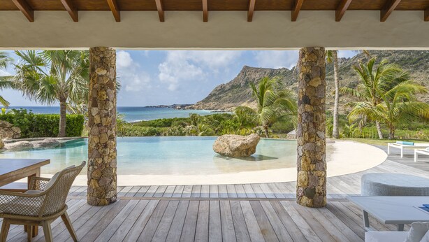 Eine Holzterrasse mit Pool, Steinpfeilern und Blick auf das Meer und die Berge.