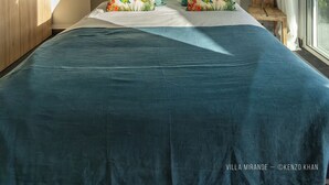 Een slaapkamer met een groot bed, een plafondventilator en een raam met gordijnen.