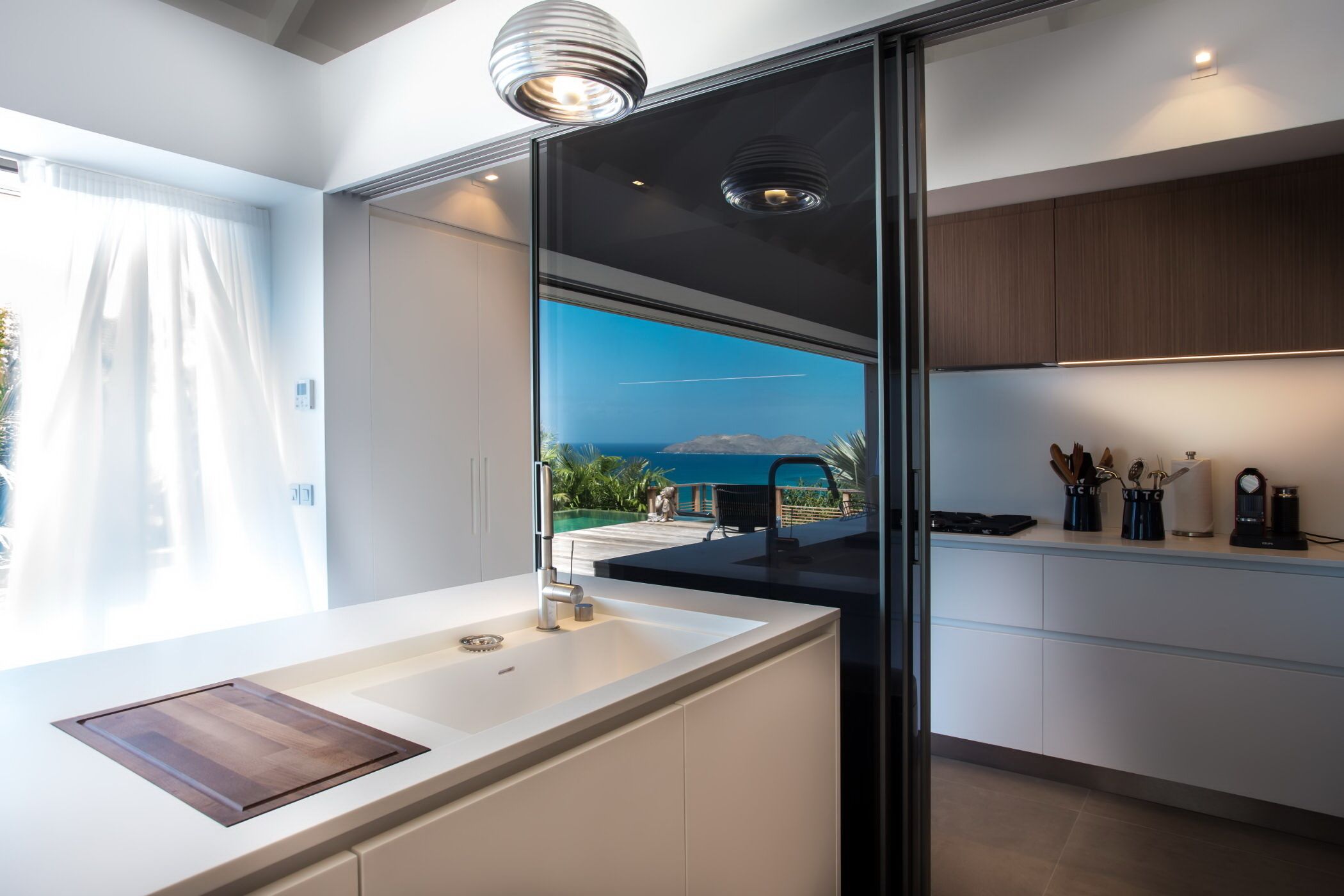 A modern kitchen with a large window, a built-in sink, and a view of the sea.