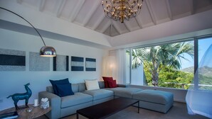 Un salon moderne avec un canapé d’angle, une table basse et une grande fenêtre donnant sur des palmiers et des montagnes.