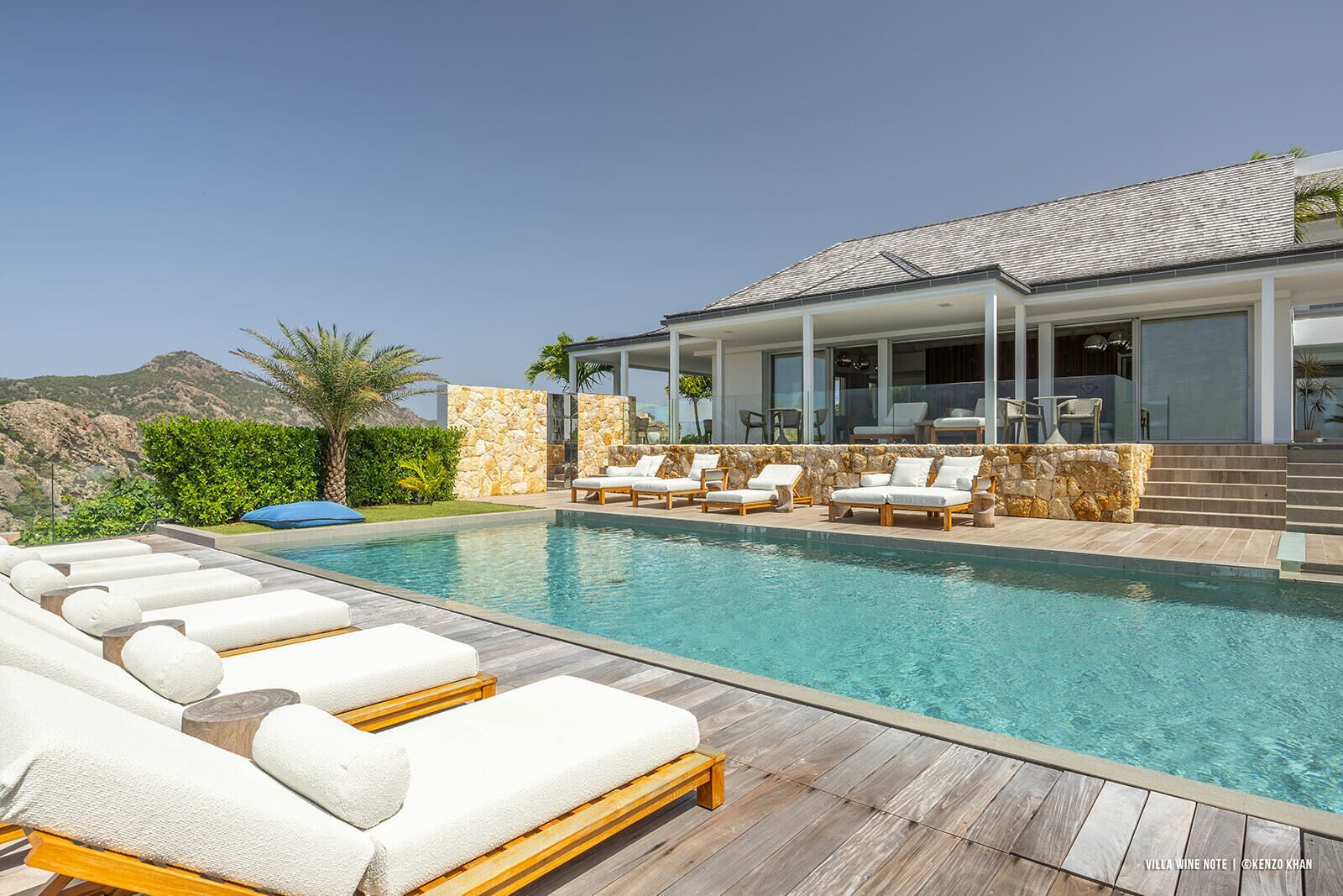 A modern villa with a swimming pool, stone walls, and a patio area with lounge chairs.