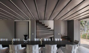 Un comedor moderno con una mesa larga, sillas blancas y una escalera que lleva a un espacio al aire libre.