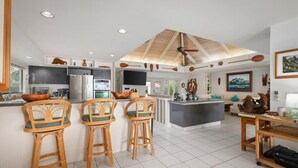 A modern kitchen with a central island, bar stools, and a ceiling fan. - Oceanfront Luxury at Alii Point | Private Pool, Panoramic Views & Tropical Serenity (Kailua-Kona)