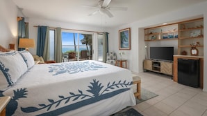 A bedroom with a large bed, a ceiling fan, a TV, and a view of the ocean through the sliding glass door. - Oceanfront Luxury at Alii Point | Private Pool, Panoramic Views & Tropical Serenity (Kailua-Kona)