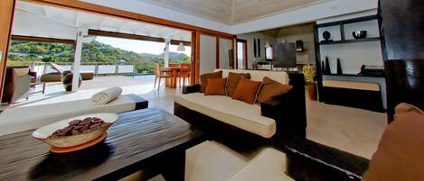 Relax in a spacious living area with a comfortable sofa, dining table, and scenic views of lush green surroundings.