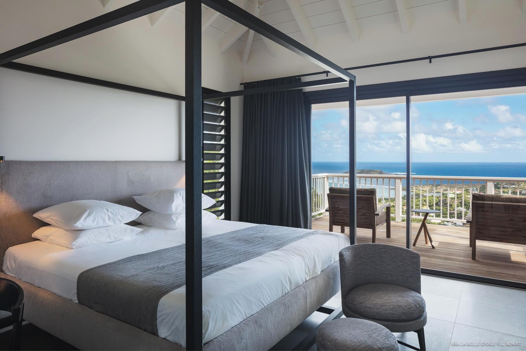 Una camera da letto moderna con un letto grande, un balcone vista oceano e un’area salotto con un tavolo.