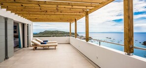 Enjoy the sea view from this balcony with a pergola overhead, featuring comfortable sun loungers and a tiled floor.