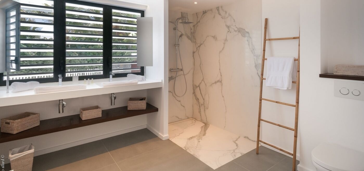 Un baño moderno con pared de ducha de mármol, lavamanos empotrado con ventana y escalera de madera.