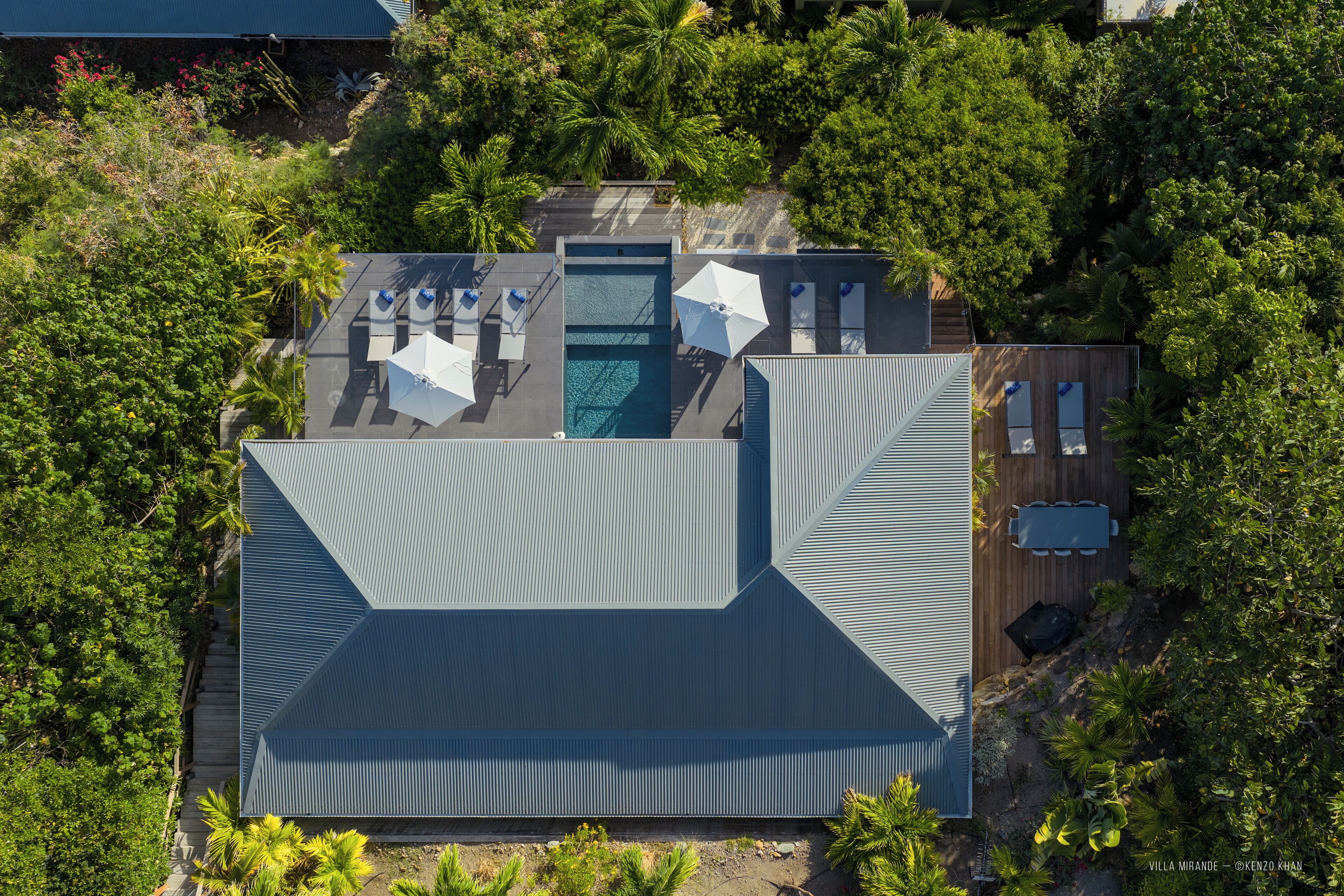 Eine Vogelperspektive eines modernen Hauses mit Swimmingpool, Sitzgelegenheiten im Freien und üppigem Grün.