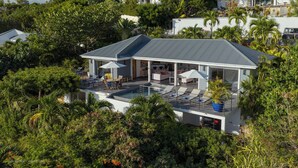 Una casa moderna con piscina, rodeada de exuberante vegetación y palmeras.
