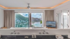Ein modernes Badezimmer mit einer großen Badewanne, einem Fernseher und Blick auf eine Küstenlandschaft.