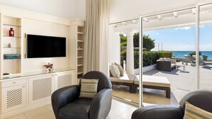 A modern living room with a flat-screen TV, a glass cabinet, and a seating area with a view of the ocean. - Villa Petite Plage 4  | Beach Front - Located in  Stunning Grand Case with Private Pool (Grand-Case)