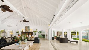A spacious living area with a high ceiling, black leather sofas, a coffee table, and a dining table. There are ceiling fans, a fireplace, and a view of the outdoors. - Villa Petite Plage 4  | Beach Front - Located in  Stunning Grand Case with Private Pool (Grand-Case)